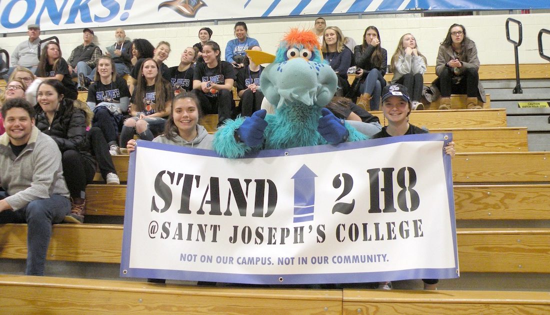 Students and Blue the mascot holding the No Hate banner during a basketball game